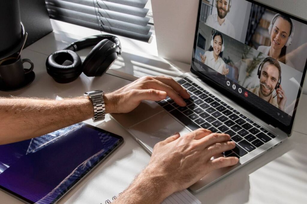 Man attending a virtual meeting with three colleagues displayed on his laptop screen at a desk.