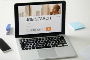 Laptop displaying a job search website with office supplies on a white desk.