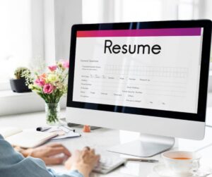 Person editing a resume on a computer screen in a bright, modern office setting.