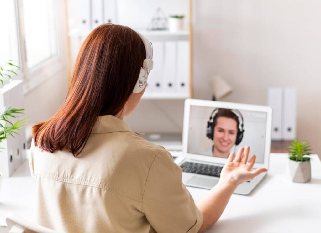 Woman with headphones using laptop for video call in a bright office.