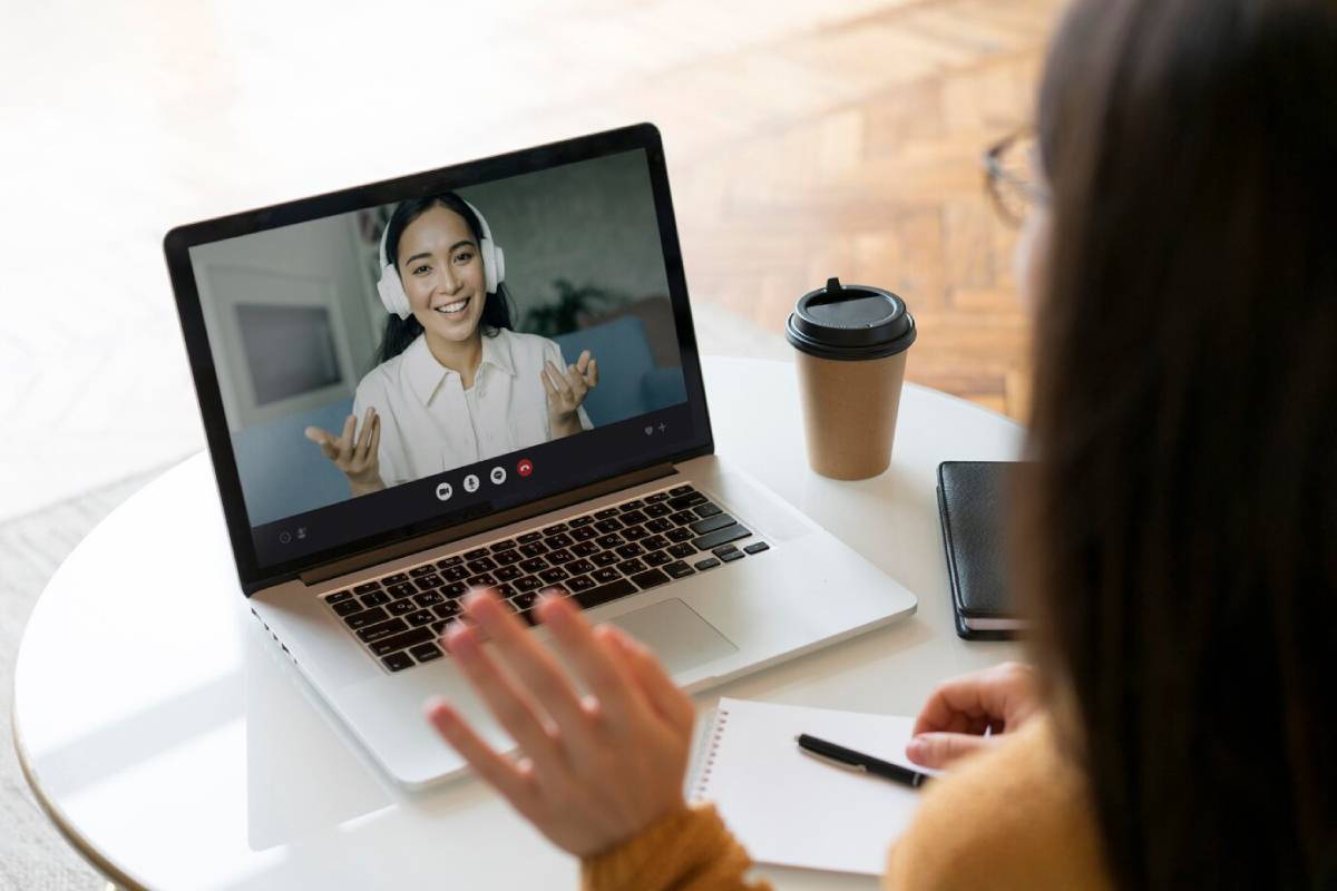  A woman participates in a video call with a smiling person wearing headphones on her laptop. 