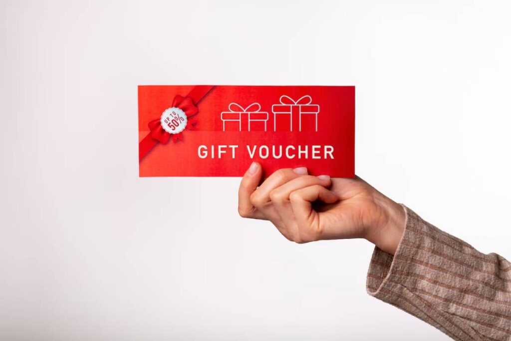 Hand holding a red gift voucher with a "up to 50%" label against a white background.