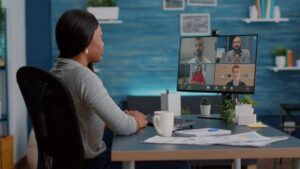 Woman participates in a virtual meeting with four colleagues displayed on her monitor in a modern office.