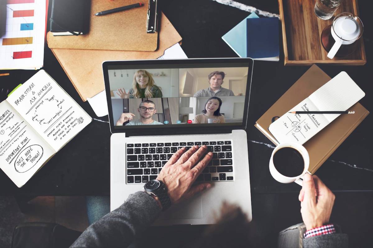 Person joining an online video meeting on a laptop surrounded by work materials and a coffee cup. 