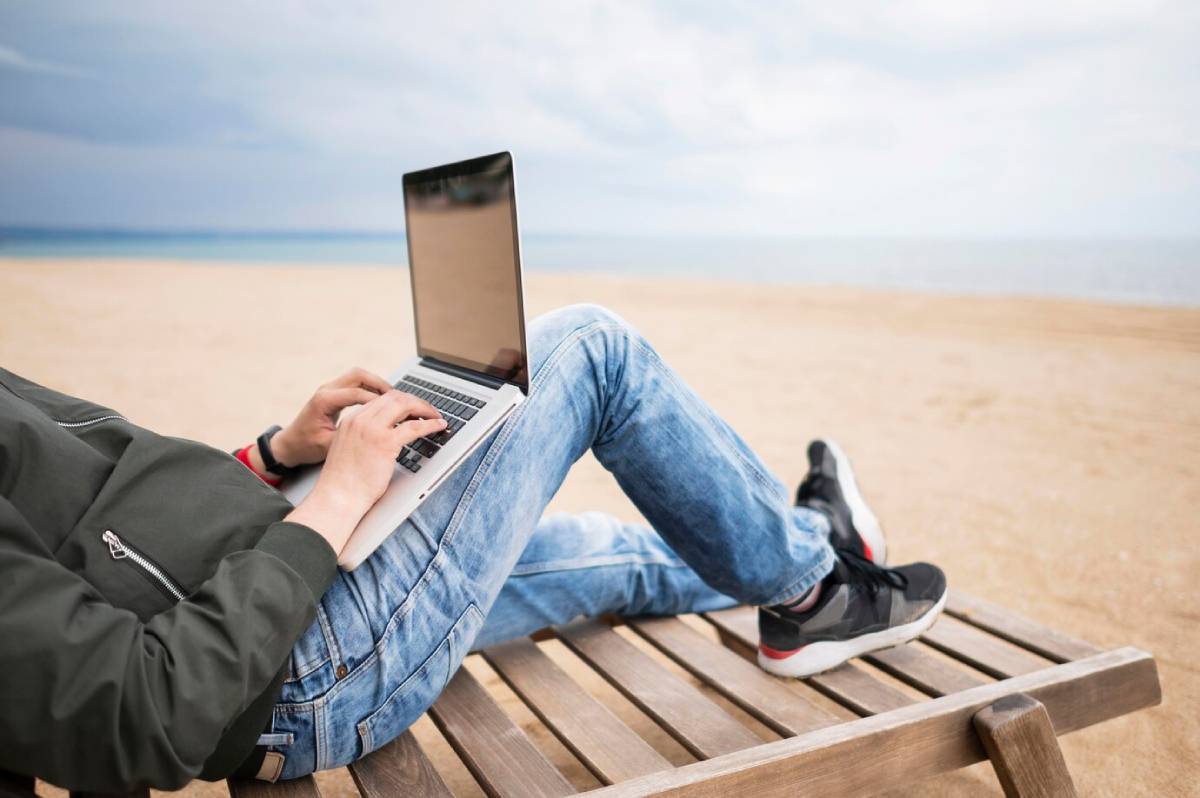  Person using a laptop on a wooden bench at the beach.