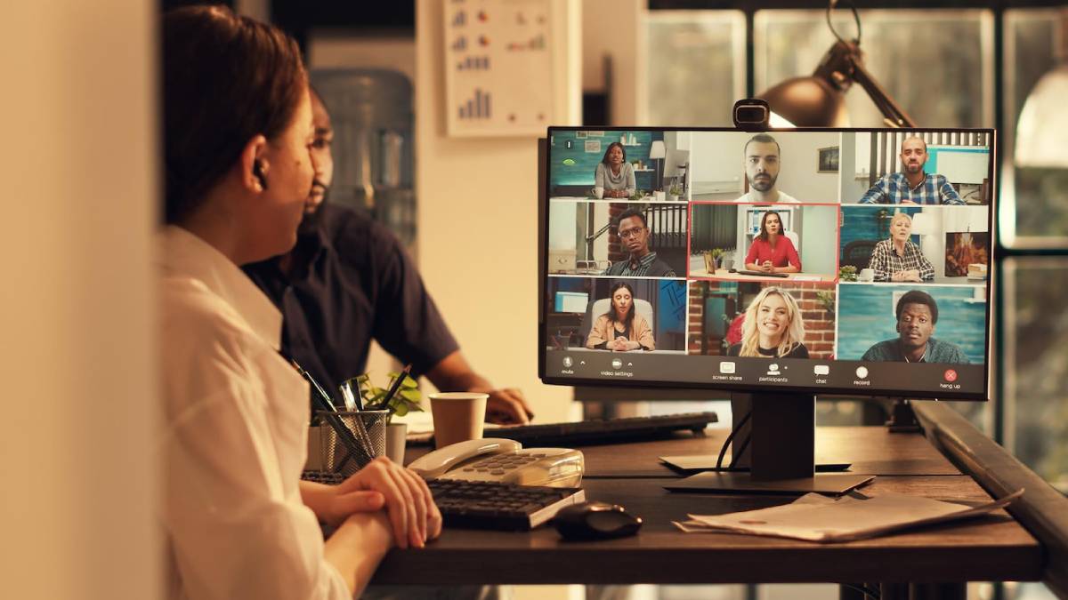  Office worker monitoring a virtual meeting with diverse participants on a computer screen.