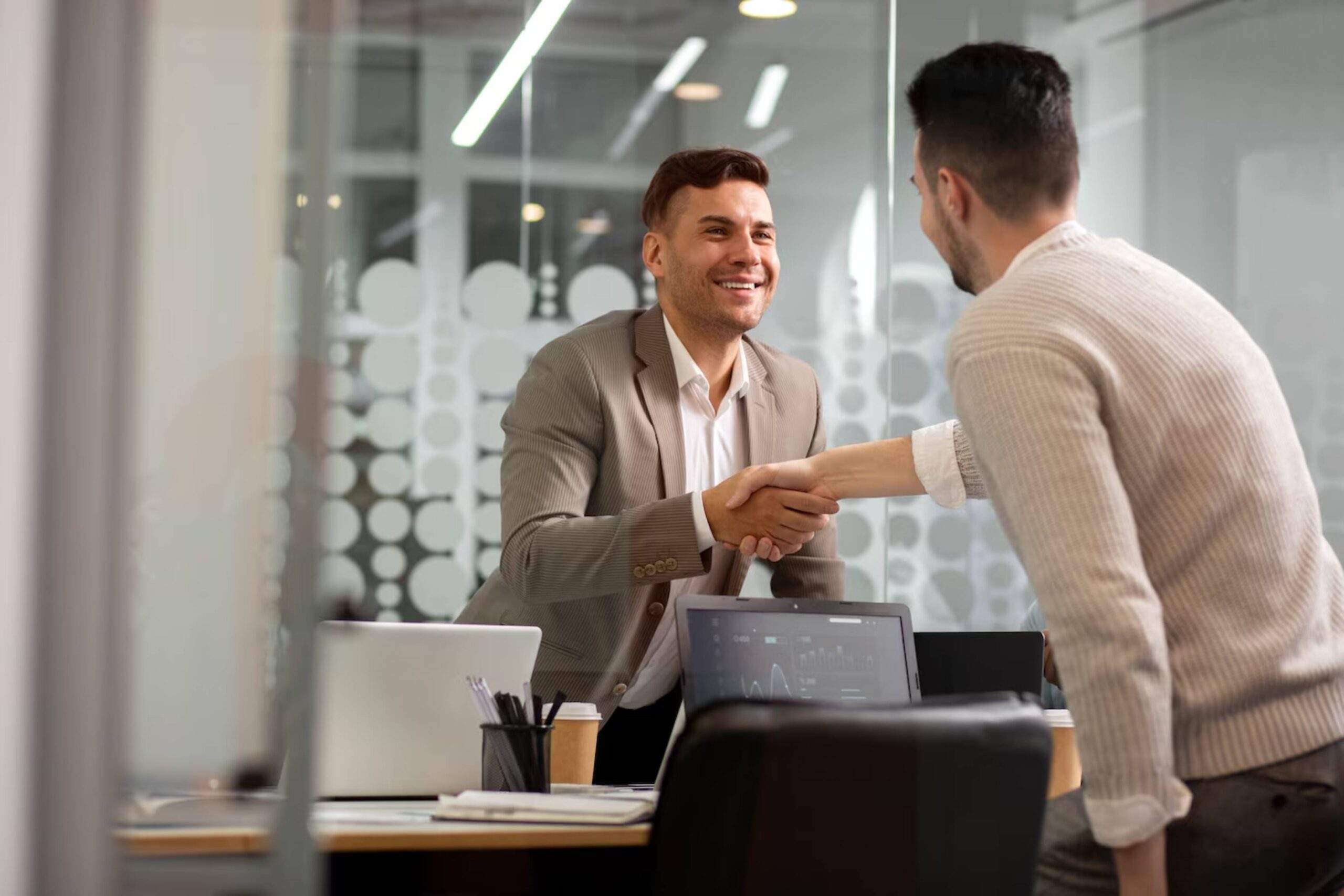 Two men shaking hands in a modern office, smiling during a meeting. 