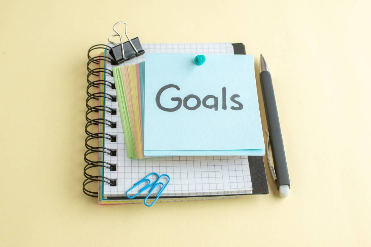 A stack of notepads and a pen on a pale yellow background, with a post-it note marked 