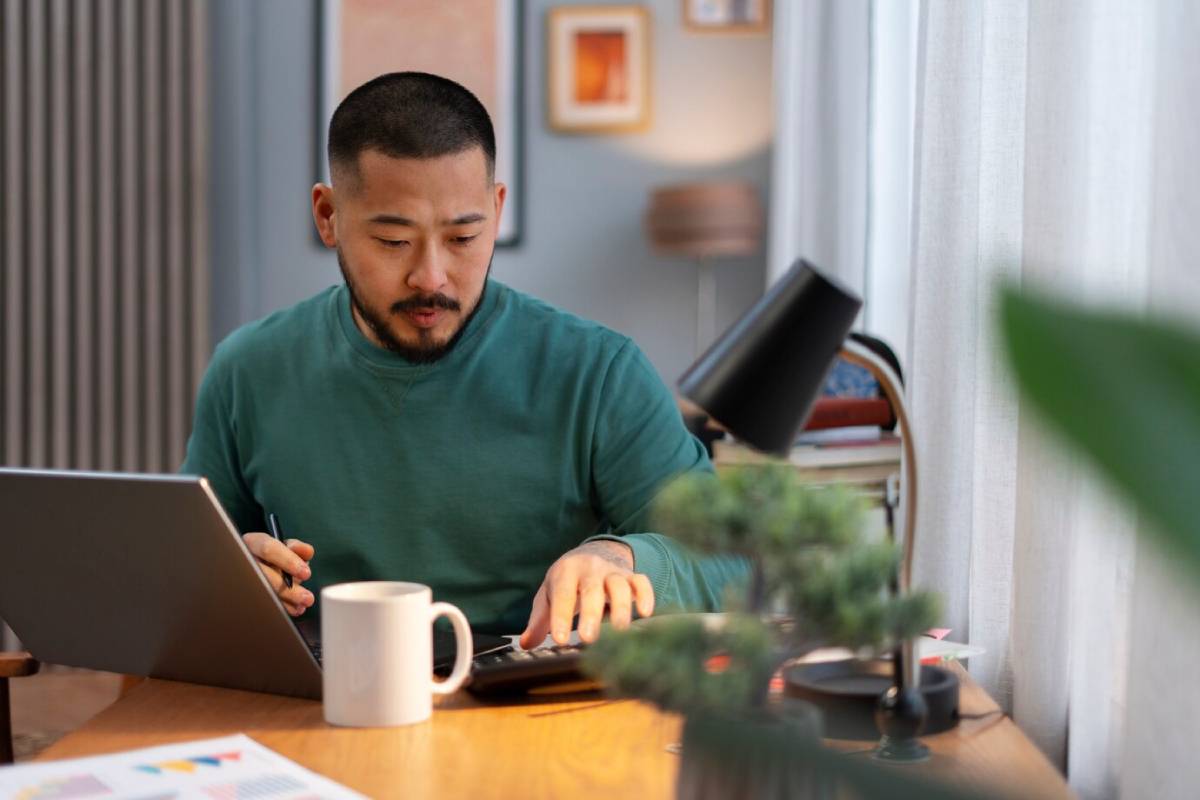 Man in green sweater focusing on work at his desk, surrounded by a cozy, well-decorated room. 