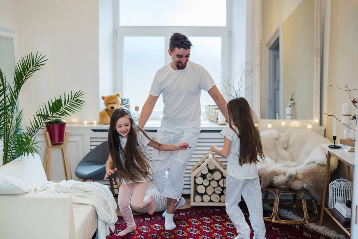  A man playing with two young girls in a cozy, well-lit living room.