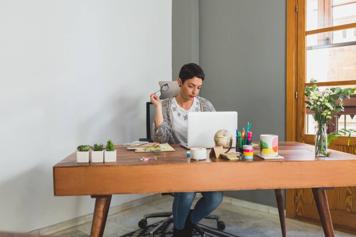 Woman working on a laptop at a tidy, well-decorated home office desk. 