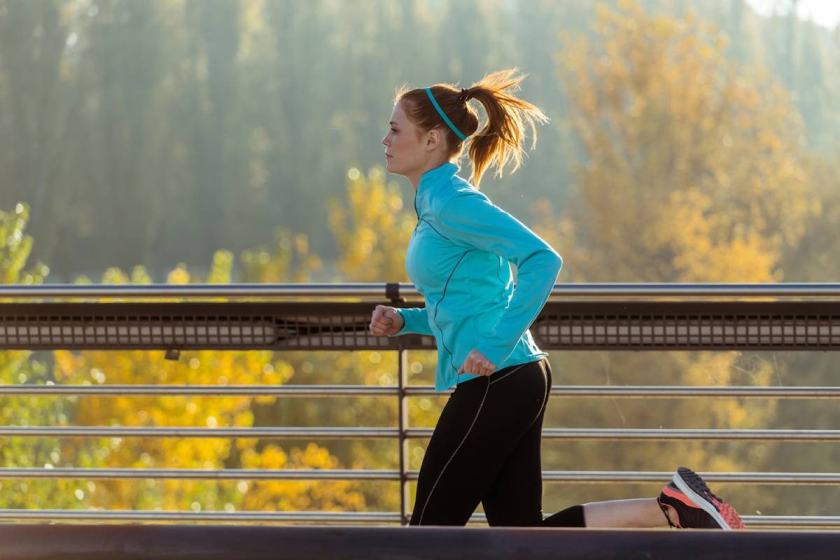  Woman in blue athletic wear jogging on bridge with autumn trees in background.