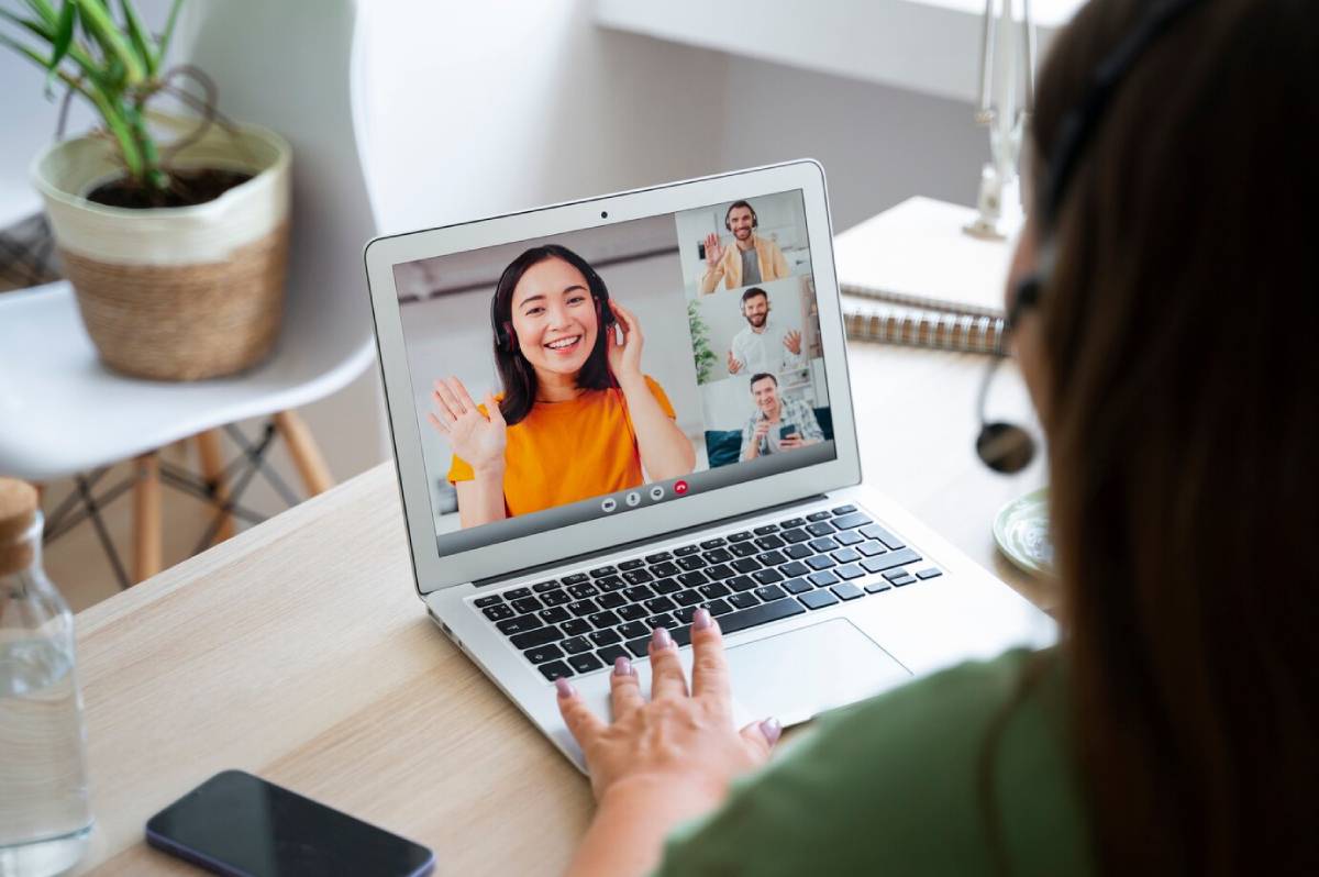 Woman in green shirt participating in a virtual meeting with three cheerful colleagues on her laptop.