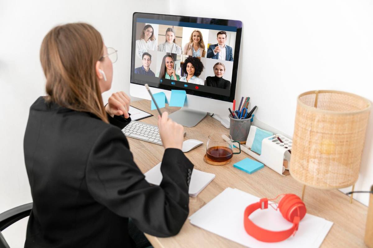 Woman in an office participating in a virtual meeting with multiple colleagues displayed on her computer screen. 