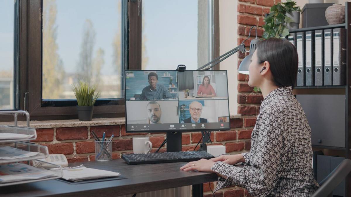 Woman in an office during a virtual meeting with four colleagues displayed on her monitor. 