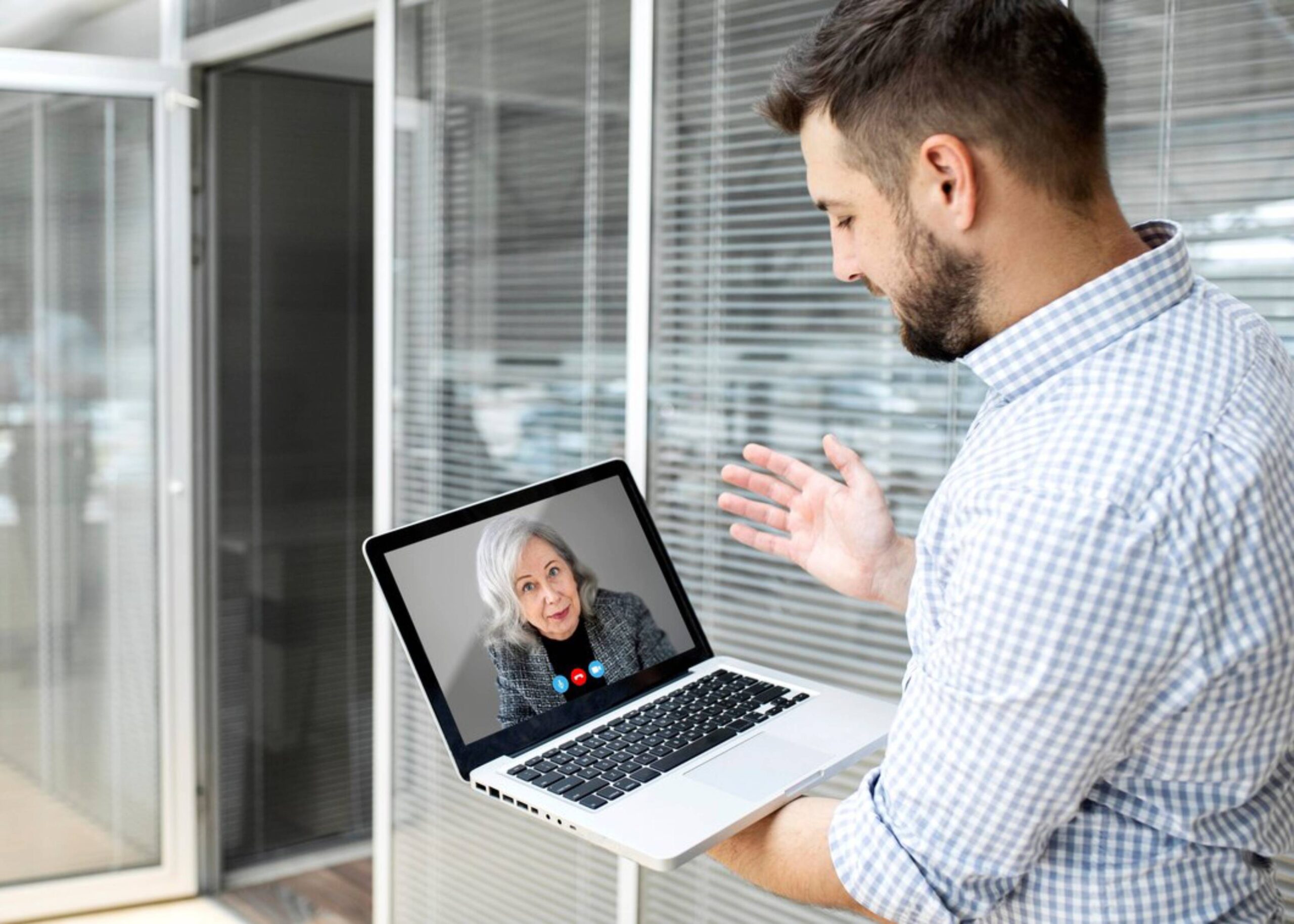  A man video chatting with an elderly woman on a laptop in a modern office setting.