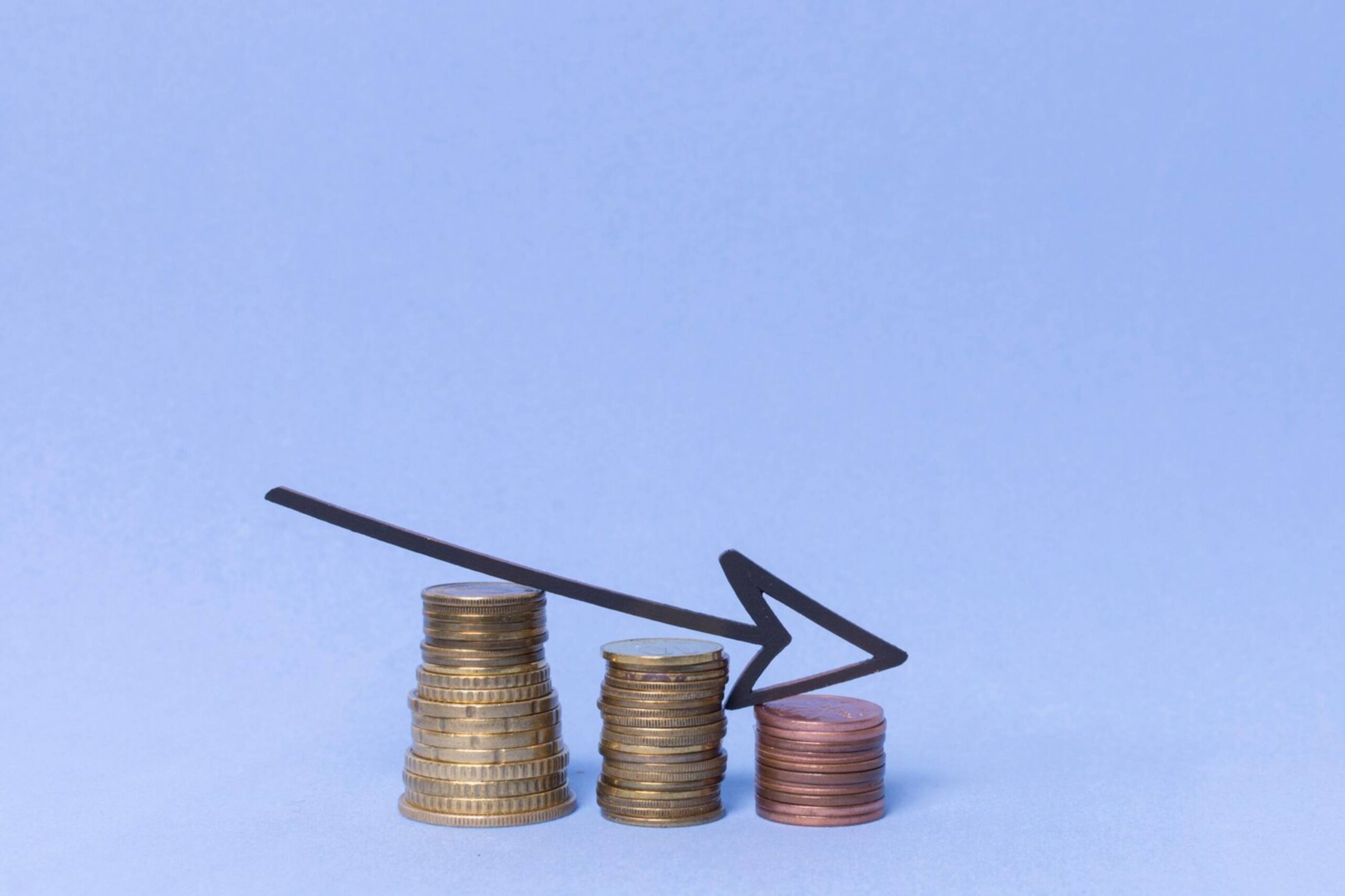  Stacks of coins with a descending arrow graph, indicating a decrease in financial value against a blue background.