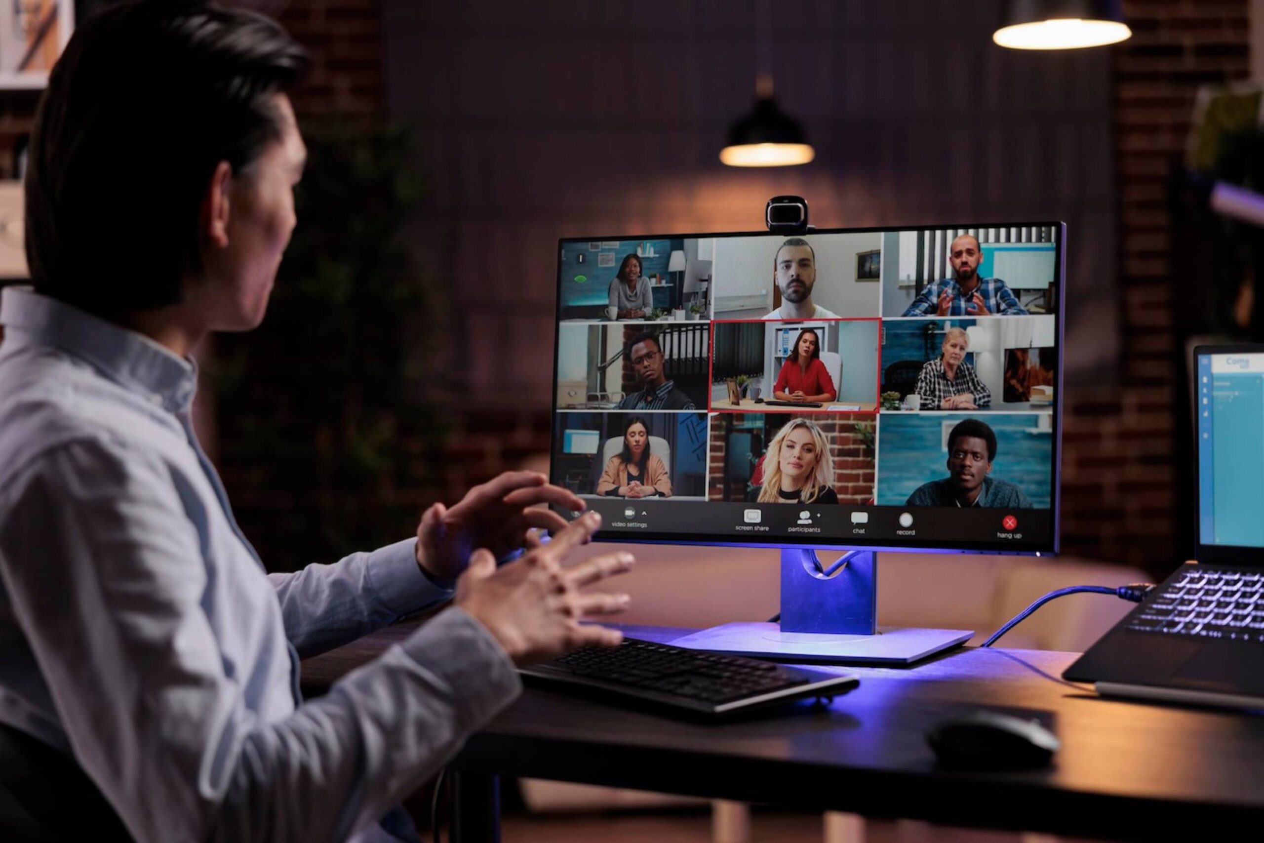  Man participates in a virtual meeting with diverse people on a monitor in a modern office.