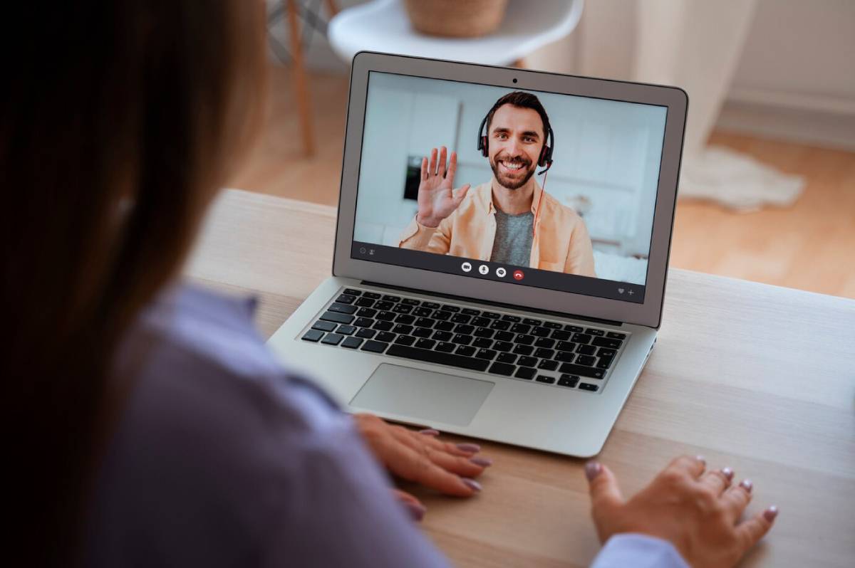 Woman in a video call with a smiling man waving hello on her laptop. 