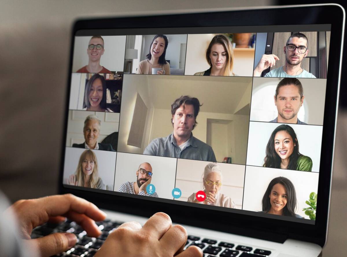 A laptop screen displaying a virtual meeting with nine diverse participants engaged in conversation. 