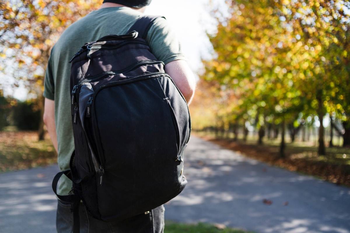 Man with backpack walking along a tree-lined path in autumn. 