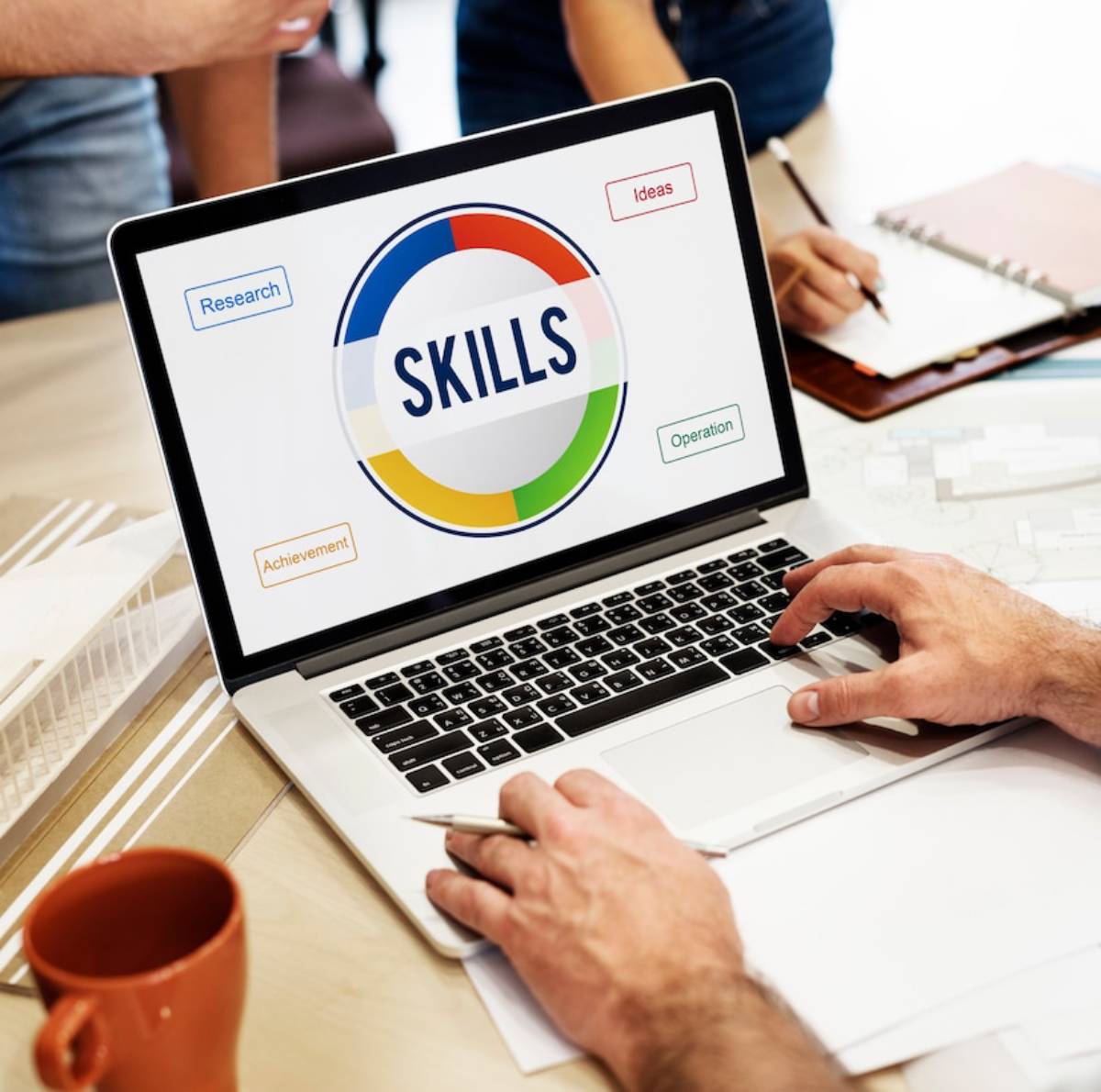 Laptop screen displaying a skills diagram during a business workshop, with participants' hands visible. 
