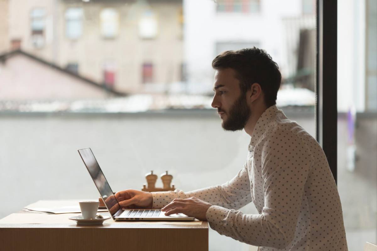 Man working on a laptop in a café with a coffee cup next to him. 