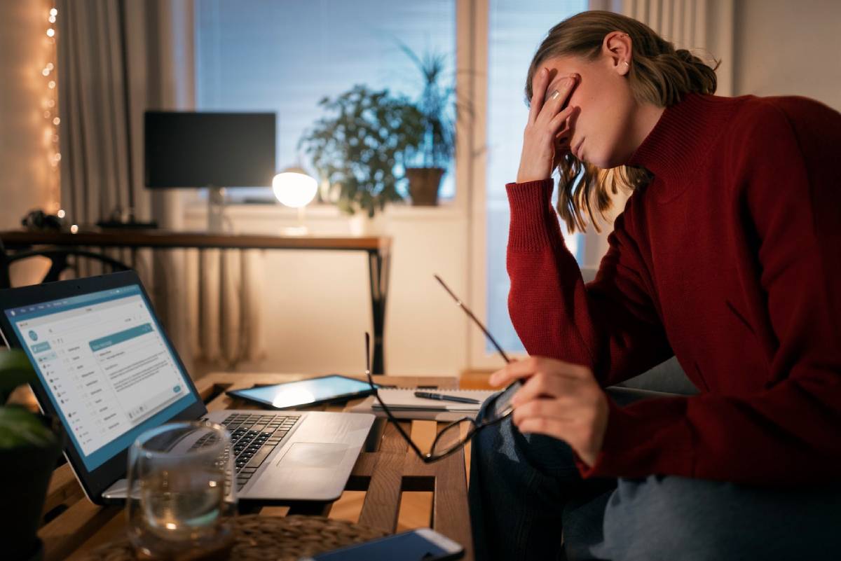  Woman stressed while working late at home with laptop and notebook on desk.