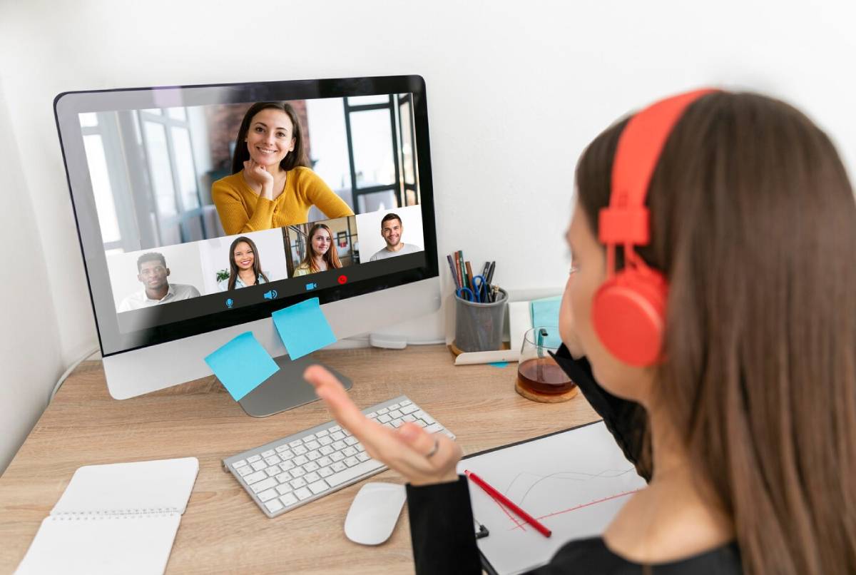 Woman with headphones participates in a virtual meeting with diverse colleagues on a computer screen. 
