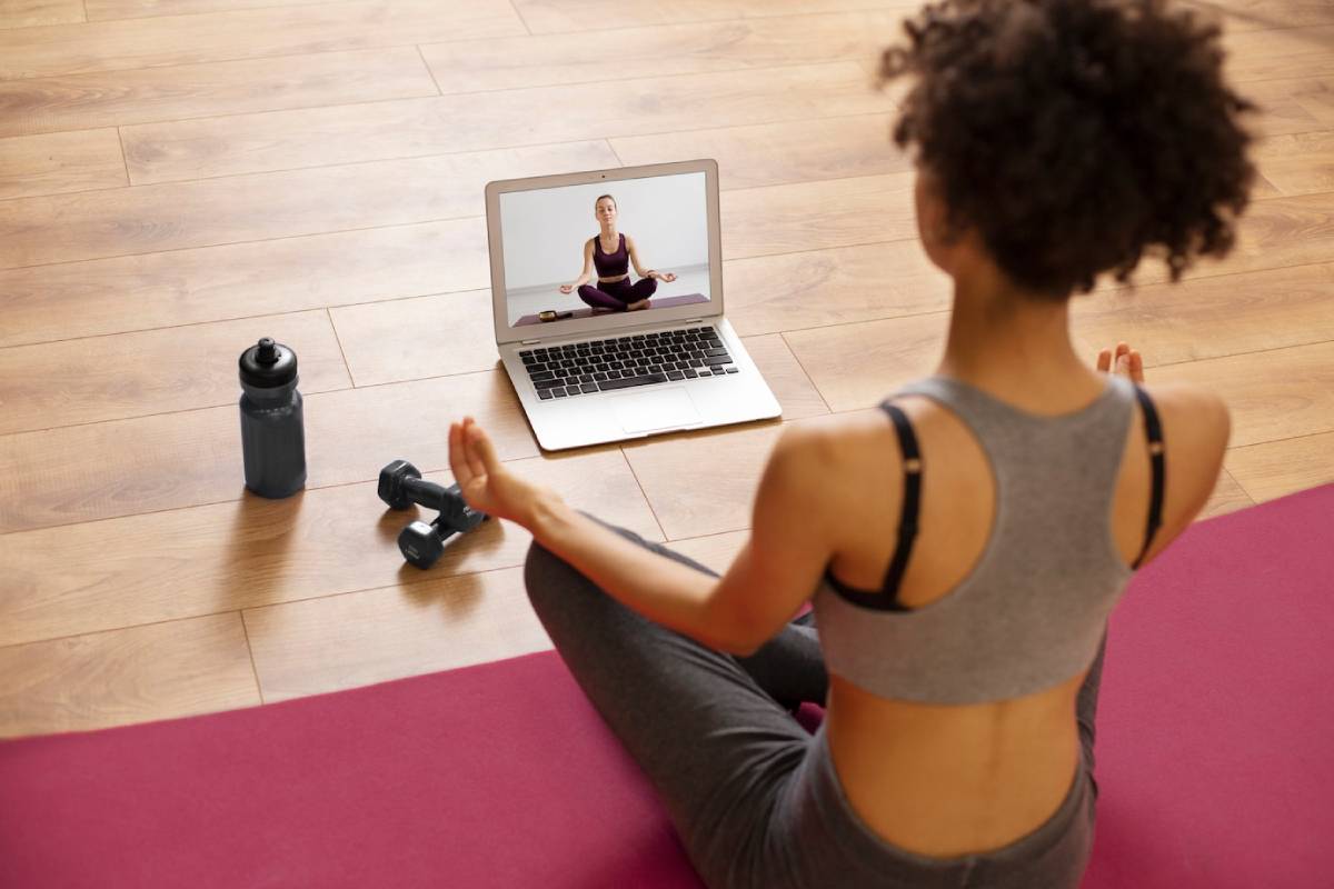 Woman practising yoga at home, following an online class on her laptop, with exercise equipment nearby. 