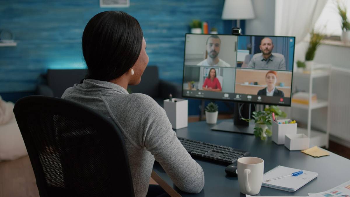Woman participates in a virtual meeting with five colleagues on a computer screen in her home office. 