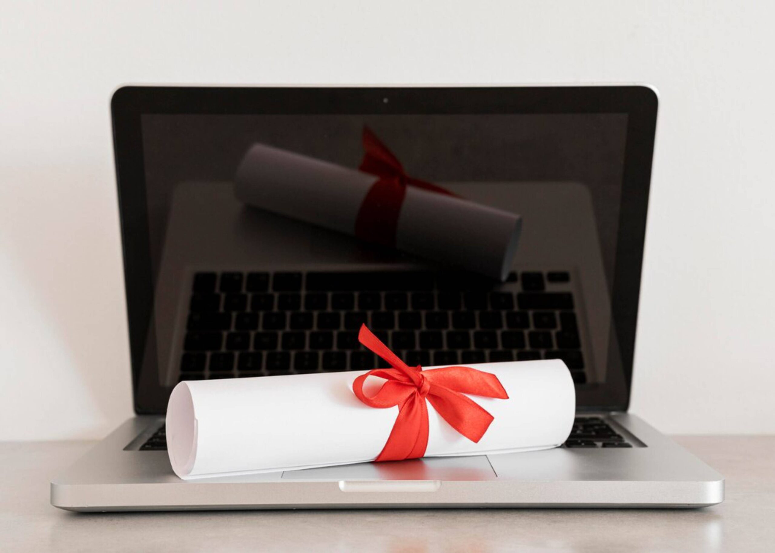  A laptop displaying a diploma wrapped with a red ribbon on its keyboard.