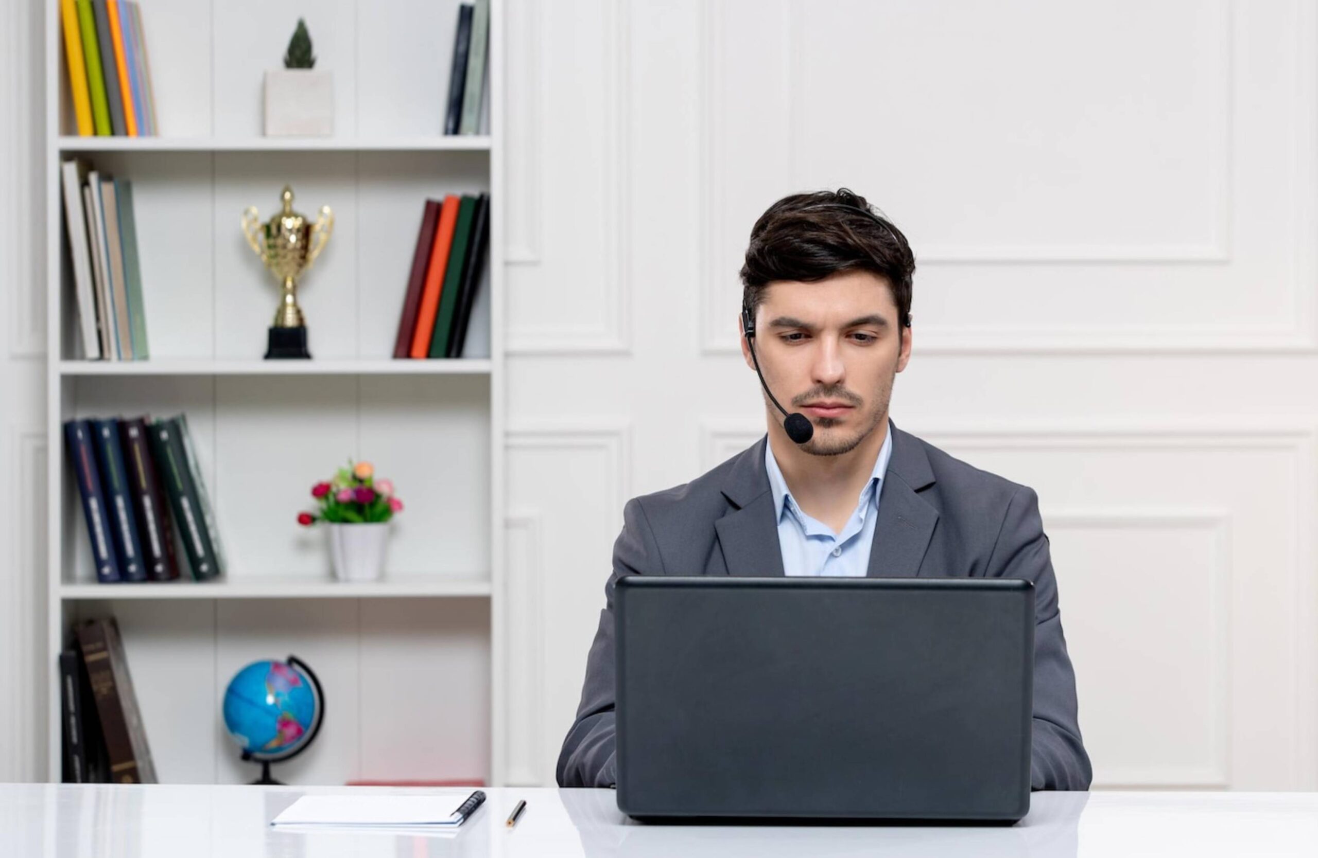  Young man with headset using laptop in a home office with a bookshelf in the background.